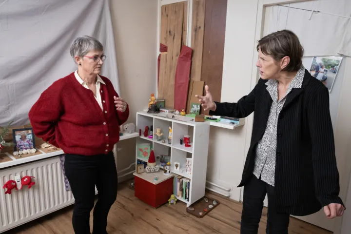 Twee vrouwen in een kamer samen in gesprek, op de achtergrond staan allerlei beeldjes in een kastje